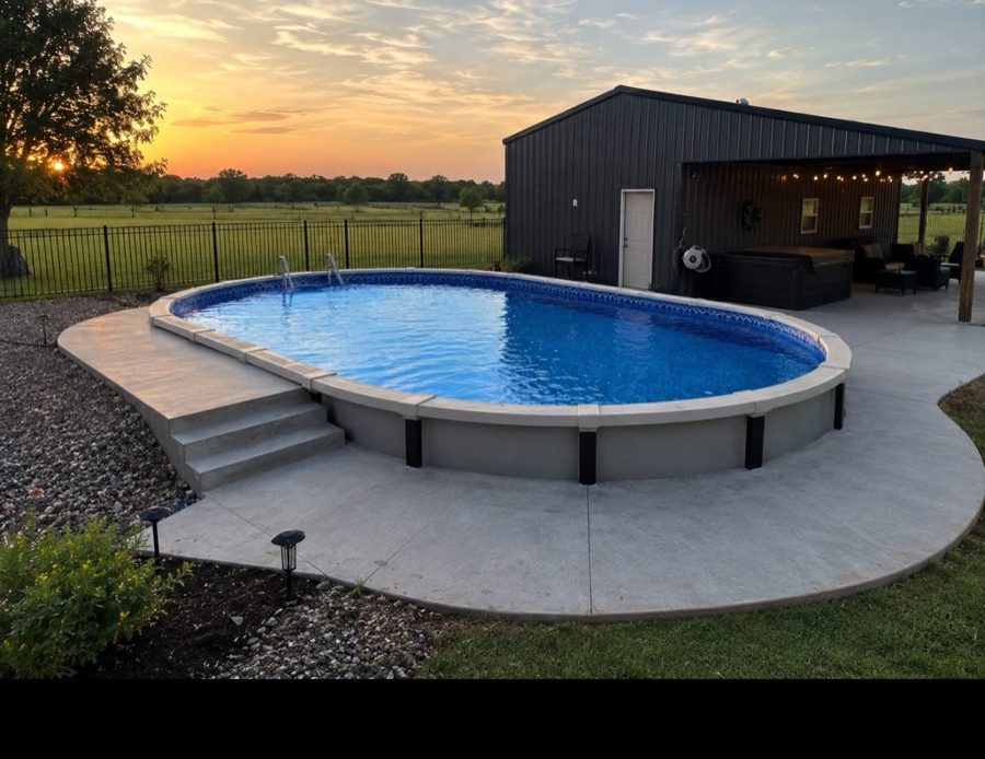 Oval vinyl inground pool with entry steps, lit for evening swimming beside a backyard barn