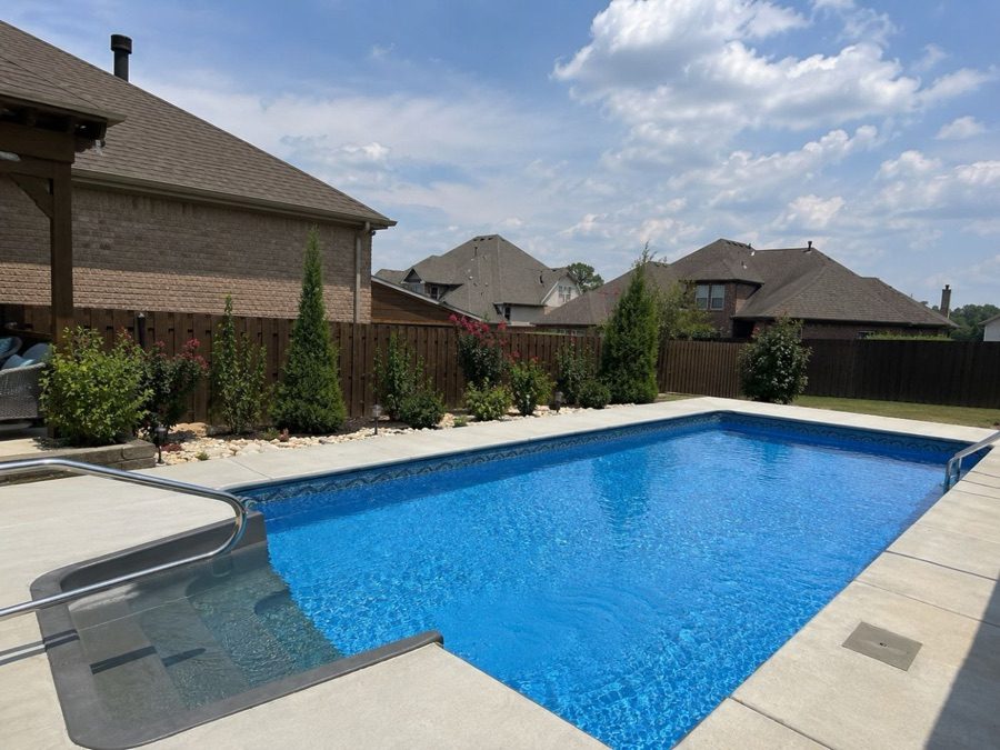 Vinyl inground pool with stainless steel entry handrail and steps beside a brick home